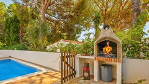 An outdoor barbecue area with a brick oven, a pool, and a wooden fence. - Spacious 4 bedroom villa with pool, near beach, ideal for families (Olhos de Água)