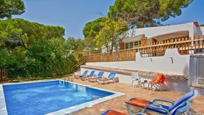 A swimming pool with blue tiles, surrounded by lounge chairs with orange cushions, and a white building with a wooden deck. - Spacious 4 bedroom villa with pool, near beach, ideal for families (Olhos de Água)