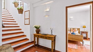 A staircase with wooden steps leading to a landing, a wooden console table with a vase of flowers, and a bed with a patterned bedspread in the background. - Spacious 4 bedroom villa with pool, near beach, ideal for families (Olhos de Água)