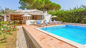 Un área junto a la piscina con piscina, sillas de descanso y una mesa con sombrillas.