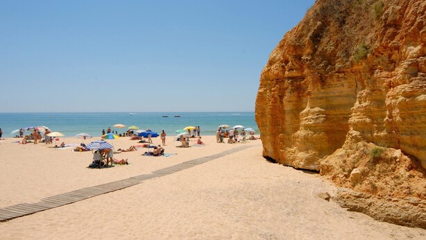 Una playa con un paseo de madera que conduce al mar, rodeada de acantilados.