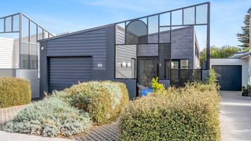 A modern two-story building with a dark exterior, a garage, and a well-maintained garden with various shrubs.