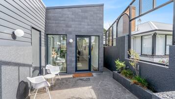 A modern house with a patio, two white chairs, and a small garden area.