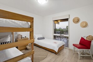A bedroom with a bunk bed, a single bed, a desk, and a chair. There is a window with a view of the outdoors.