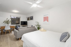 Quarto moderno com cama, sofá, escrivaninha, televisão e ventoinha no teto.