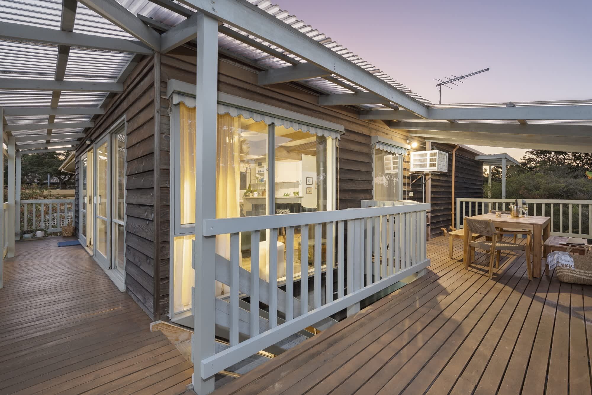 A wooden deck with a covered area, a dining table, and a white railing.