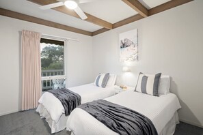 A bedroom with two beds, a ceiling fan, a window with curtains, and a painting on the wall.