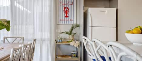 A modern kitchen with a white refrigerator, a dining table with chairs, and a kitchen island with a plant and a basket.