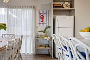 A modern kitchen with a white refrigerator, a dining table with chairs, and a kitchen island with a plant and a basket.