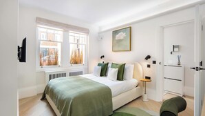 Un dormitorio con cama, mesitas de noche, una ventana y una puerta.