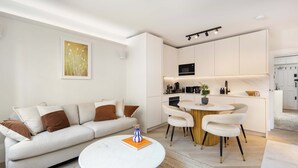 Una sala de estar moderna con sofá, mesa de centro y un comedor con sillas y una pequeña cocina.