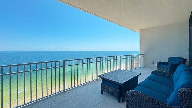 A balcony with a view of the ocean, wicker furniture, and a tiled floor.