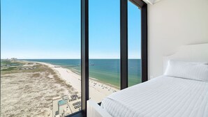 A hotel room with a large window offering a view of a beach and ocean.