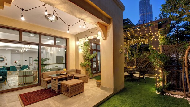 An outdoor patio area with wicker furniture, string lights, and a view of a tall building in the background. - Durrani Homes - Arabian luxury at Souk Al Bahar besides Burj Khalifa & Dubai Mall (Dubai)
