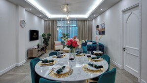 A modern dining room with a round table set for four, a chandelier, and a large window with curtains. - Durrani Homes - Arabian luxury at Souk Al Bahar besides Burj Khalifa & Dubai Mall (Dubai)