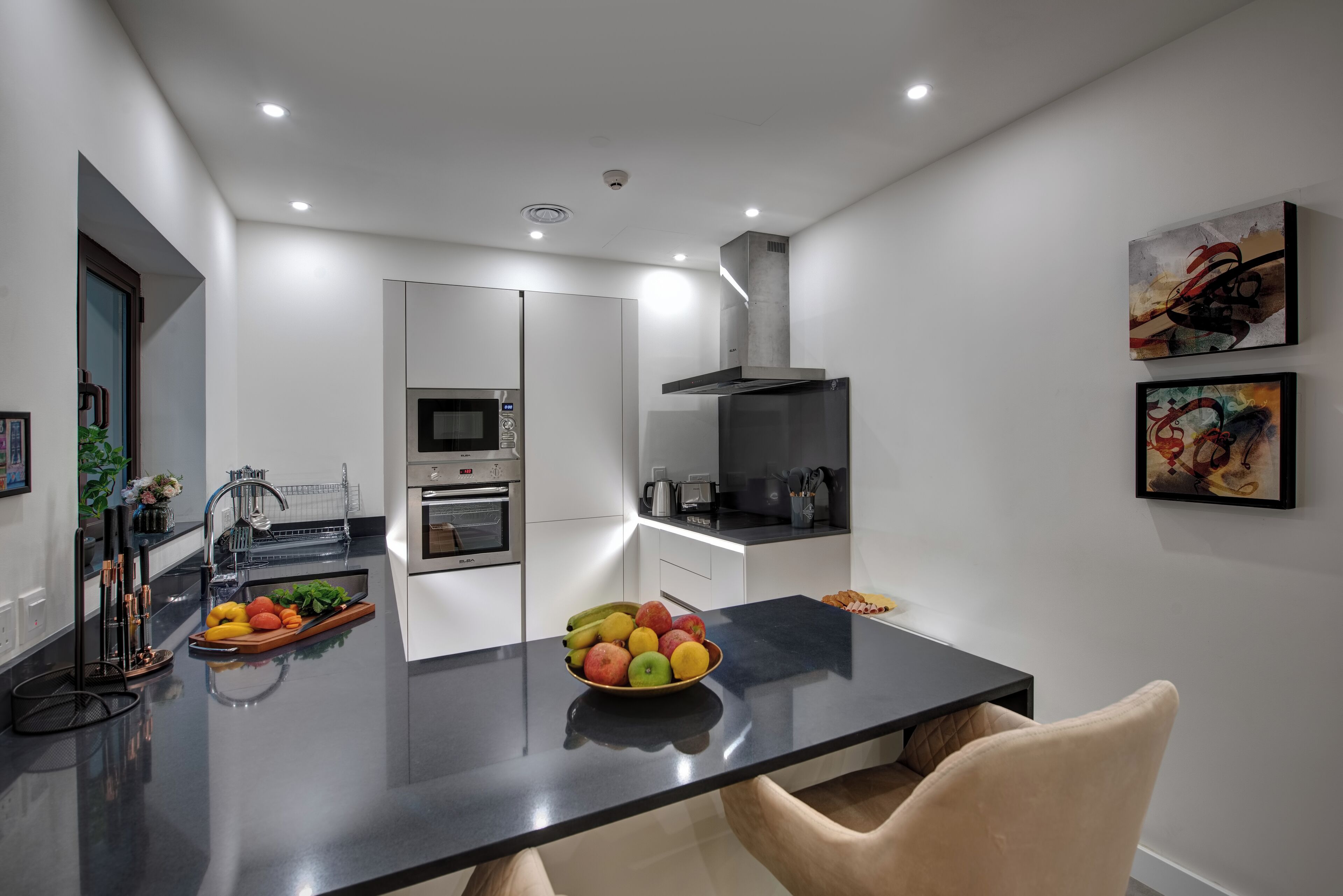 A modern kitchen with a black countertop, white cabinets, and a bowl of fruit.