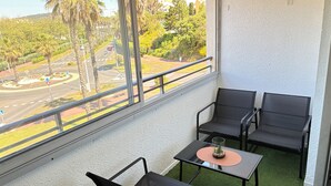 Un balcon avec deux chaises et une table, donnant sur une route bordée de palmiers et traversée par un rond-point.