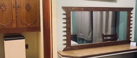 A bedroom with a wooden wardrobe, a small refrigerator, a mirror with a wooden frame, and a television mounted on the wall.