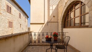 Un pequeño patio al aire libre con una mesa redonda y dos sillas, una planta en maceta y una cesta de fruta.