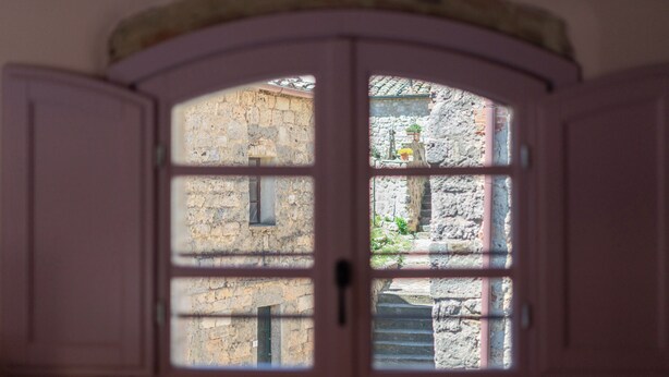 Vista a través de una ventana que muestra un muro de piedra y una escalera en el exterior.