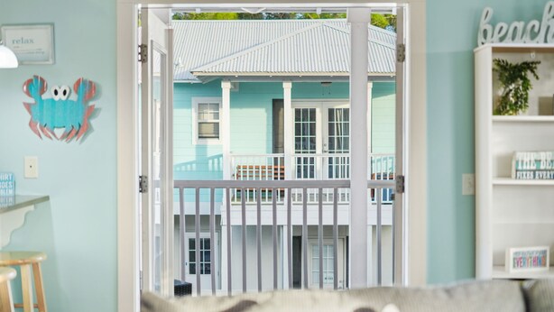 A view through a door into a room with a light blue wall, a white door, and a small balcony with a white railing. - Pet-Friendly PCB Vacation Rental | Pool | Walk to Beach (Panama City Beach)