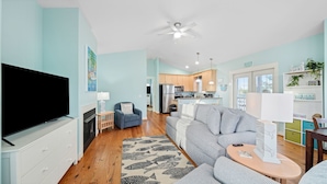 A modern living room with a flat-screen TV, a grey sofa, a patterned rug, and a kitchen in the background. - Pet-Friendly PCB Vacation Rental | Pool | Walk to Beach (Panama City Beach)