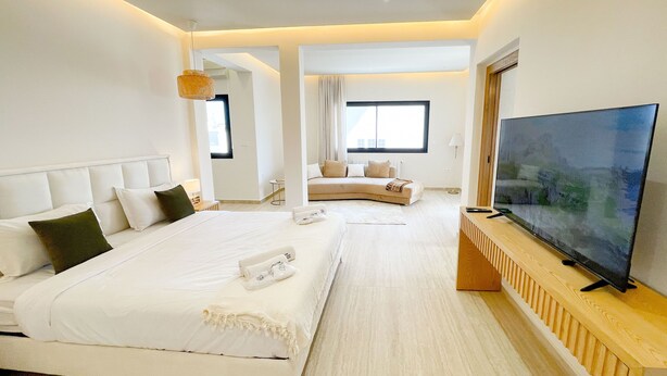 A modern hotel room with a large bed, a TV, and a view of the city.