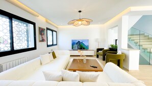 A modern living room with a white sofa, a coffee table, a TV, and a staircase.