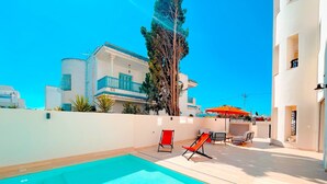 A rooftop pool area with a clear blue pool, lounge chairs, and a view of surrounding buildings.