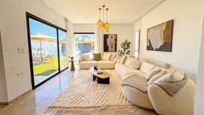 A modern living room with a large sectional sofa, a coffee table, and a view of a garden through large windows. - Villa Alba Luxe et Confort a Hammamet (Hammamet)