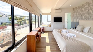 A modern bedroom with a large bed, a wooden bench, a TV, and a view of the city. - Villa Alba Luxe et Confort a Hammamet (Hammamet)