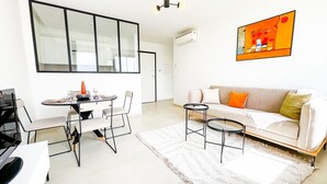 A modern living room with a white sofa, a dining table with chairs, a coffee table, and a large window. - Petit Cocon Neuf et Styl la Marsa (La Marsa)