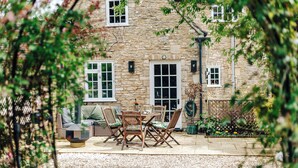 A stone building with a patio area featuring a table and chairs, surrounded by plants and a garden. - NEW luxury historic apartment, private garden, parking, dog-friendly, in Tetbury (Tetbury)