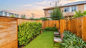 Un patio trasero con cerca de madera, césped cuidado y un espacio de estar con una silla.