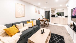 Una sala de estar moderna con un sofá gris, una mesa de centro de madera y un comedor con una pequeña mesa y sillas.