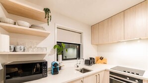 Una cocina moderna con microondas, tostadora y pileta. Se observan placares de madera y un ventanal sobre la pileta.