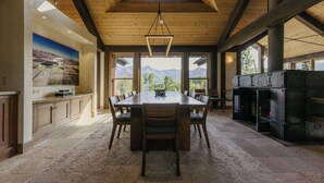 Une salle à manger spacieuse, dotée d’une grande table et de chaises en bois, d’un sol en pierre et offrant une vue sur les montagnes grâce à de grandes fenêtres.