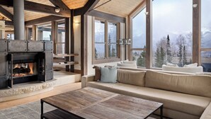 Un salon spacieux doté d’une cheminée, de grandes fenêtres et offrant une vue sur les montagnes.