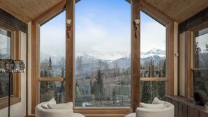 Une pièce chaleureuse avec de grandes fenêtres donnant sur les montagnes, des poutres en bois au plafond et une petite table.