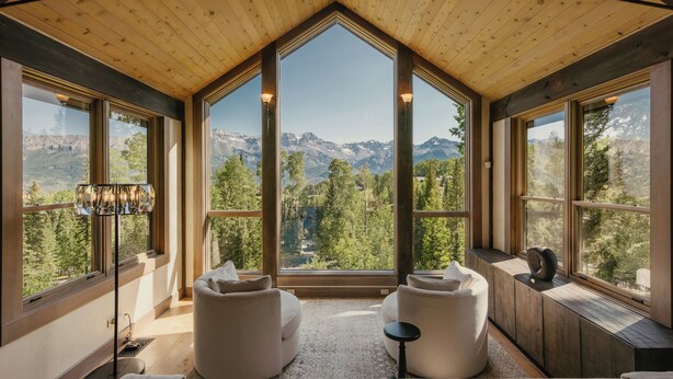 Un intérieur moderne avec de grandes fenêtres offrant une vue sur les montagnes, un coin salon confortable avec deux canapés et une petite table, et un plafond en bois.