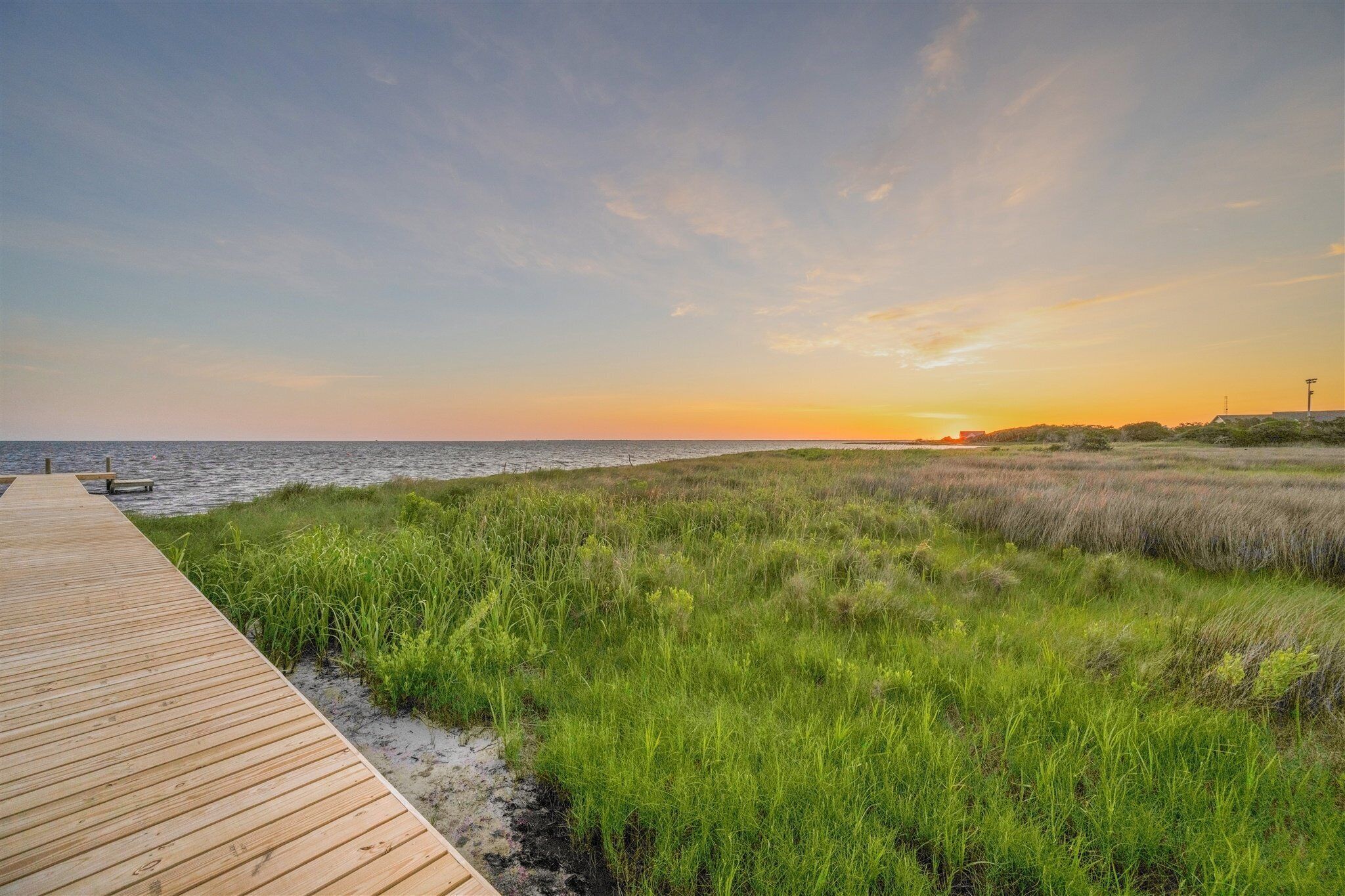 A wooden pier extending into a grassy area with a sunset in the background.