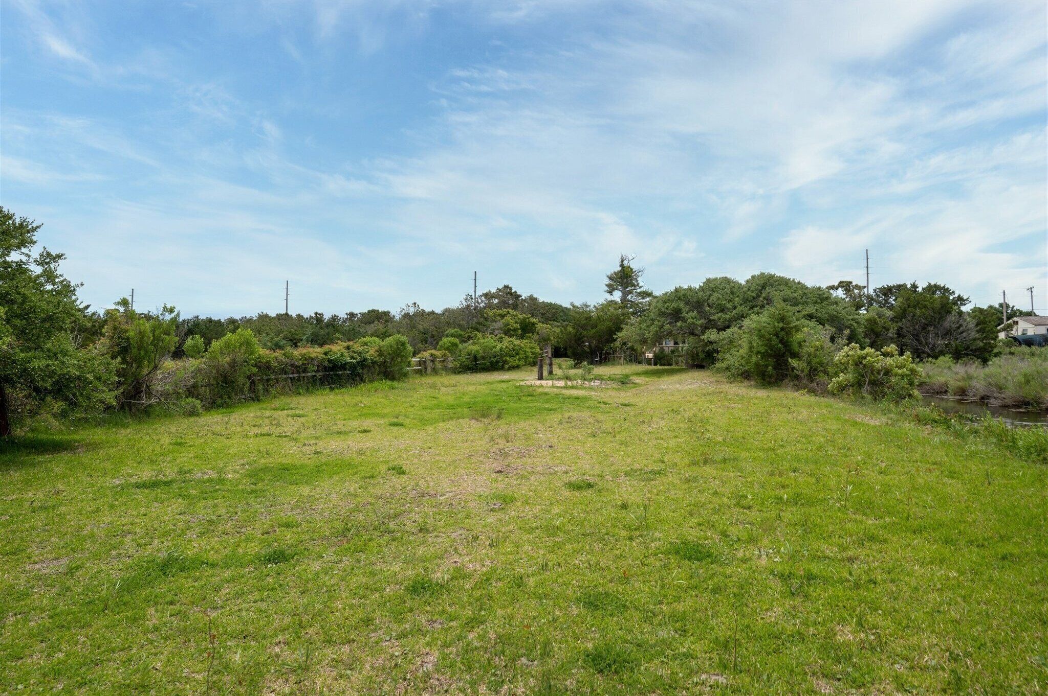 A grassy field with trees and a fence in the background.