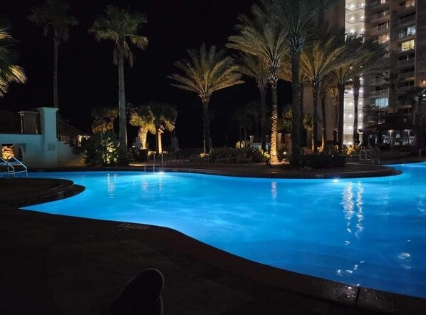 A nighttime swimming pool with palm trees and a building in the background. - Shores Of Panama 412 1 Bedroom Condo (Panama City Beach)