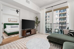Relax in this stylish living room with a large flat-screen TV, green sofa, and balcony with city views.