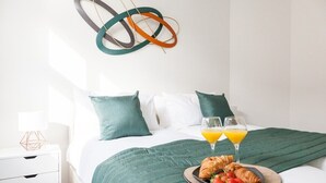 A neatly made bed with a green blanket, two pillows, a tray with croissants and strawberries, and two glasses of orange juice.