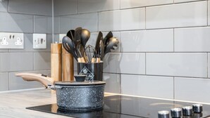 A modern kitchen with a black induction cooktop, a stainless steel pot, and a utensil holder with various kitchen tools.