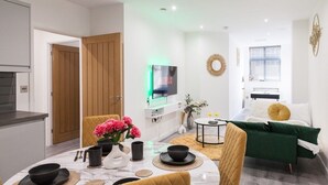 A modern living room with a dining area, a TV mounted on the wall, and a green sofa.