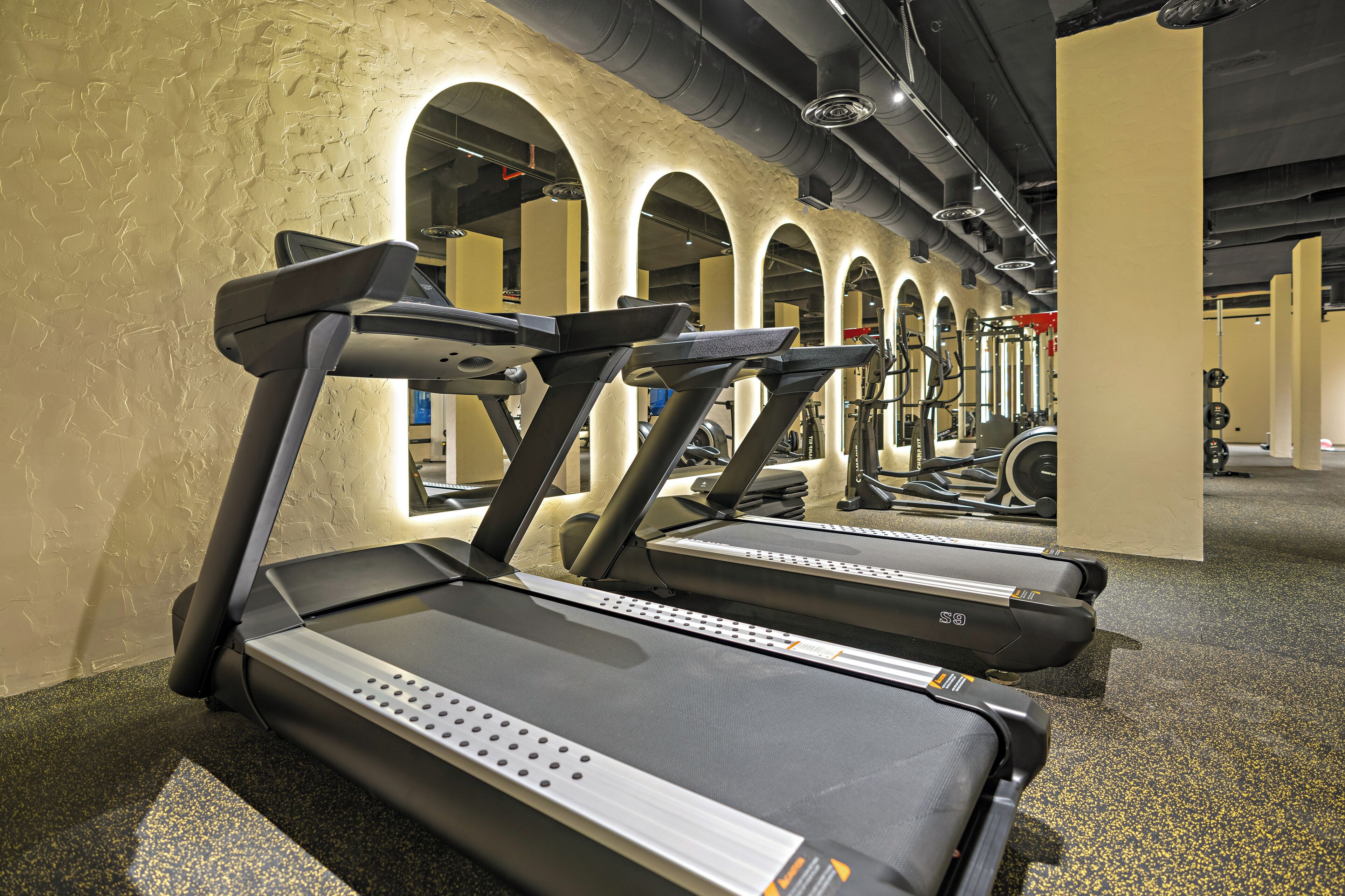 A row of treadmills in a gym with a textured wall and arched ceiling.