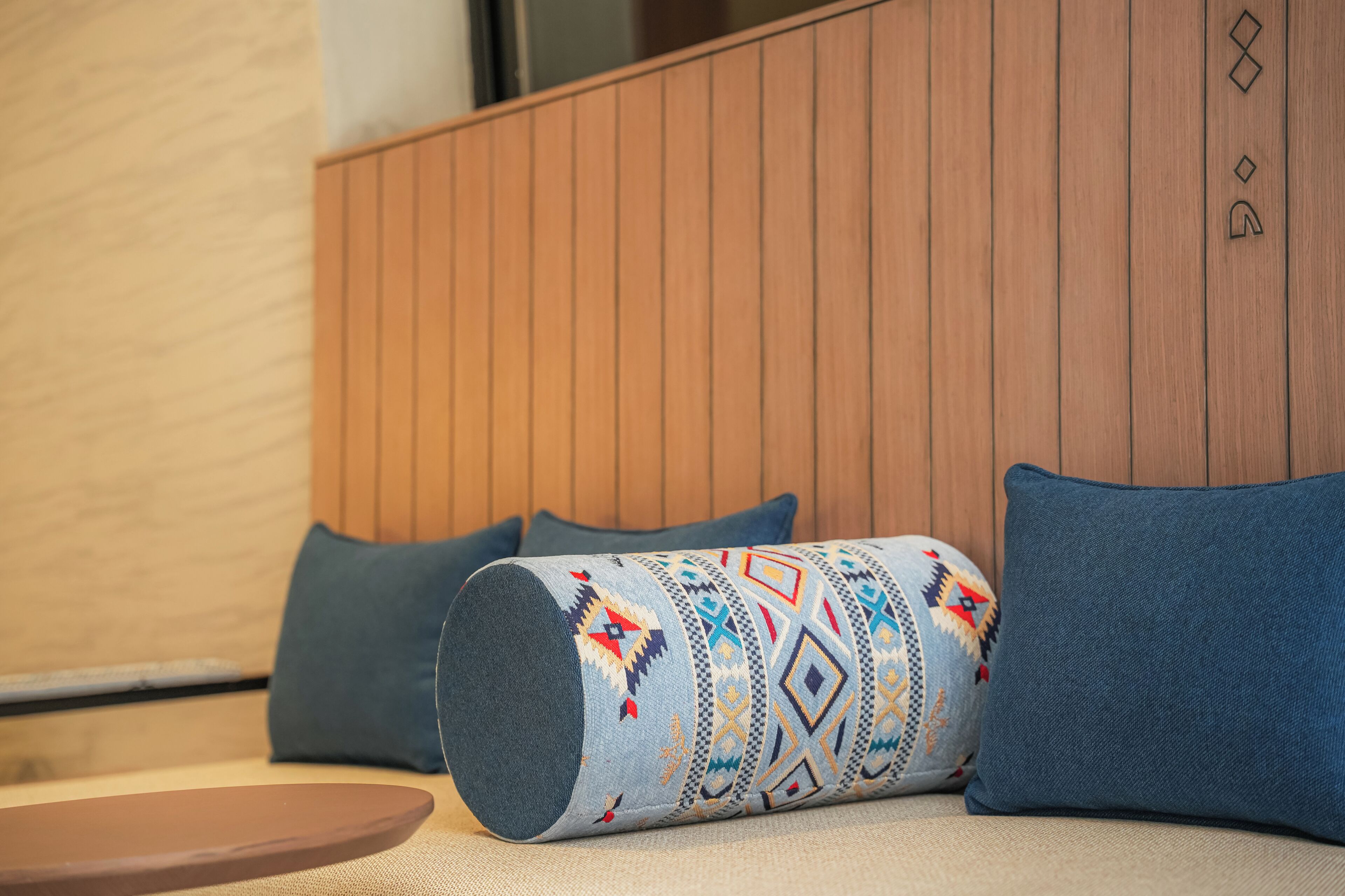 A room with a wooden panel wall, a patterned cushion, and a blue pillow.
