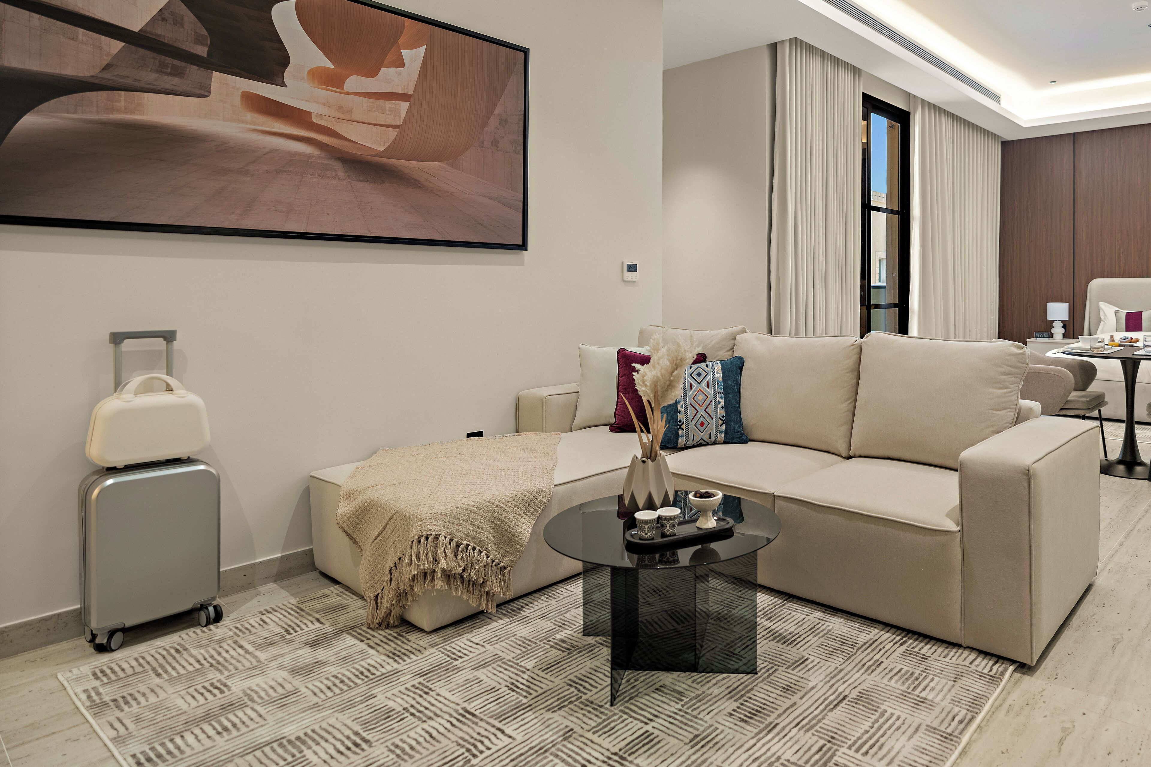 A modern hotel room with a sofa, a coffee table, a suitcase, and a large abstract painting on the wall.